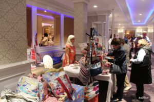 A lively scene at the 2024 Autumn Craft and Gift Fair in Ballyconnell, showing vendors interacting with customers inside the Slieve Russell Hotel. The room is filled with tables showcasing handcrafted items, jewelry, and decorations.